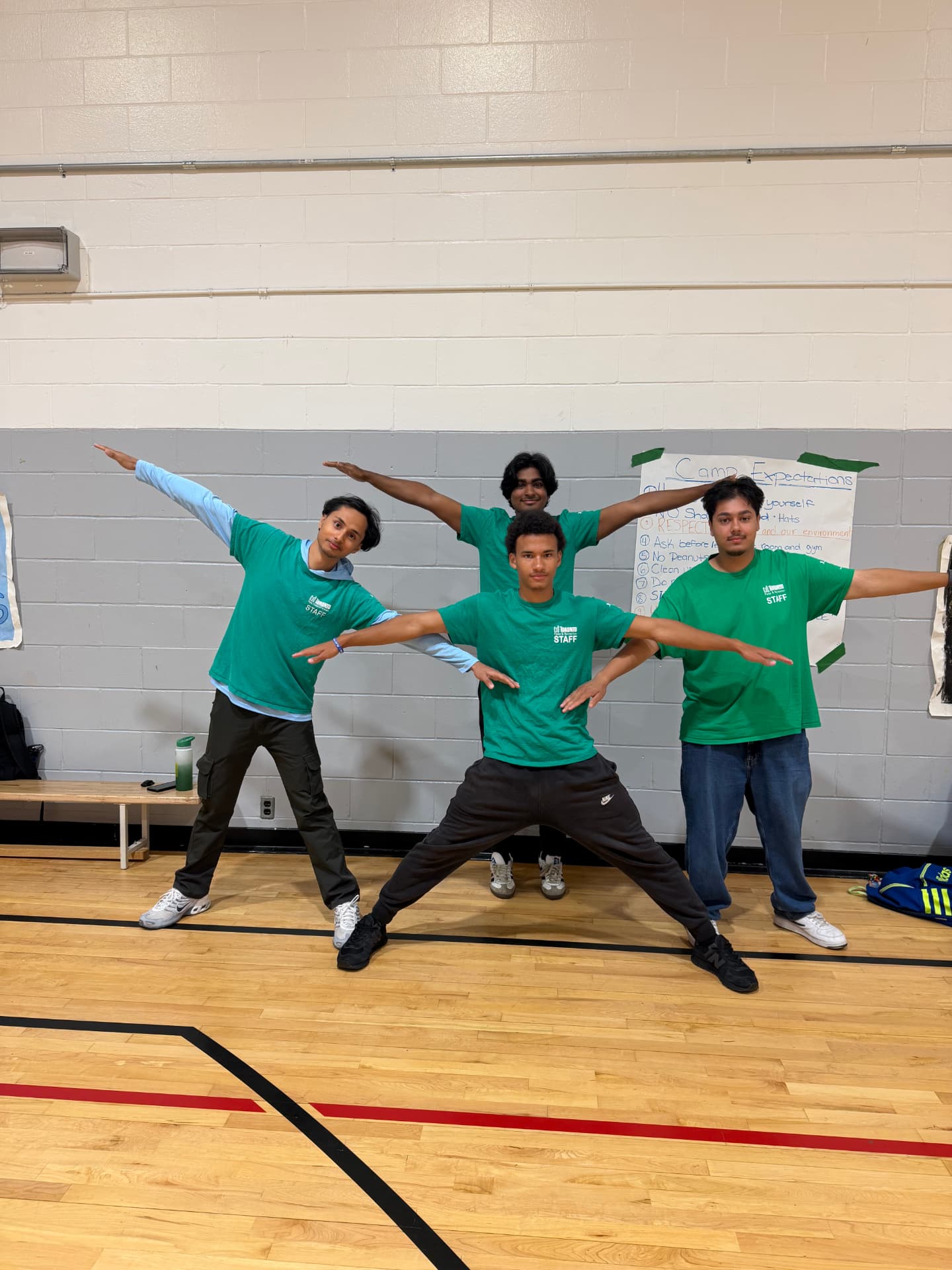 Four camp staff in green shirts holding the iconic outstretched-arm T-pose stance